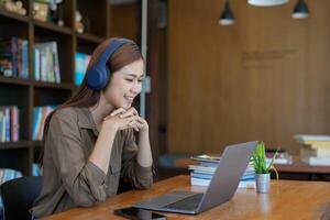 Asian tutor of language start online lesson with trainee wave hand smiling looks at pc screen. woman in headphones communicating distantly, e-learning process, application usage concept photo
