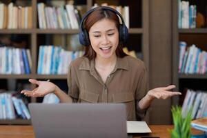 Asian tutor of language start online lesson with trainee wave hand smiling looks at pc screen. woman in headphones communicating distantly, e-learning process, application usage concept photo