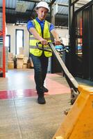 Asian male warehouse worker pulling a pallet truck. Worker working with hand pallet truck unloading cargo boxes on pallet at the warehouse. photo
