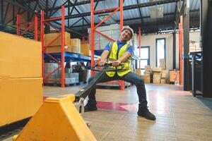 Asian male warehouse worker pulling a pallet truck. Worker working with hand pallet truck unloading cargo boxes on pallet at the warehouse. photo