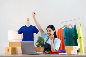Happy exciting successful asian woman doing clothing business selling online. she using laptop computer. online sell marketing delivery, SME e-commerce telemarketing concept photo
