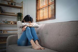 joven solitario atractivo asiático mujer llorando en sofá sensación triste cansado y preocupado sufrimiento depresión aislado a hogar. mental salud y aislamiento, estrés, desempleo y desconsolado concepto. foto