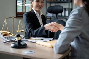 Gavel Justice hammer on wooden table with judge and client shaking hands after adviced in background at courtroom, lawyer service concept. photo