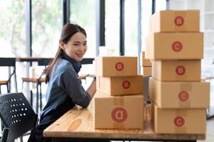 SME entrepreneur Small business entrepreneurs Online selling ideas, Happy Young Asian business owner work on computer and a boxes at home, delivery SME procurement package box deliver to customers photo