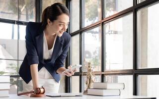 female lawyer in strict suit works in office or court, checks clients' contracts, chats by phone. .Asian womansuccessful business lady, statuette of Themis, goddess of justice. legal advice online photo