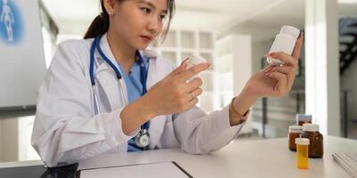 Female doctor writing in a notebook and holding a medicine bottle works at a computer while there were many medicine bottles on the table while sitting at a work desk photo