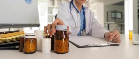 Female doctor writing in a notebook and holding a medicine bottle works at a computer while there were many medicine bottles on the table while sitting at a work desk photo