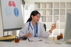 Female doctor writing in a notebook and holding a medicine bottle works at a computer while there were many medicine bottles on the table while sitting at a work desk photo