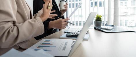 Business team and two colleague discuss data from graph financial chart and document use laptop to contact negotiations. Planning on the office desk, startup business concept photo