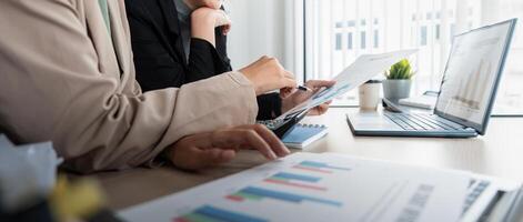 Business team and two colleague discuss data from graph financial chart and document use laptop to contact negotiations. Planning on the office desk, startup business concept photo