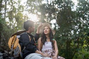 Cheerful romantic lesbian couple traveler with backpacks on their backs go hiking through the forest and siting relaxing while hiking in the mountains photo