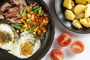 Fried eggs with vegetables, fried bacon and potatoes. Hearty food and a delicious lunch. photo