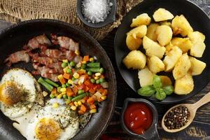 Fried eggs with vegetables, fried bacon and potatoes. Hearty food and a delicious lunch. photo