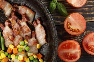 Fried bacon with vegetables and tomatoes in a pan. photo