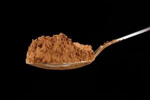 Cocoa powder on a spoon on black close-up photo
