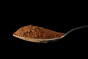 Cocoa powder on a spoon on black close-up photo