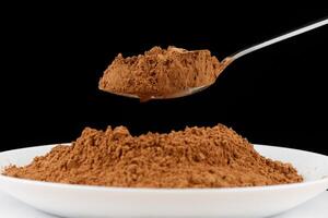 Cocoa powder on a spoon on black close-up photo