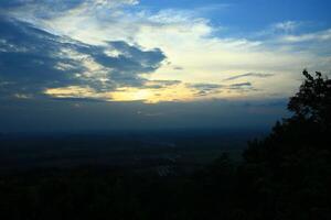 A landscape natural scenery in the form of a forest on a hill at sunset with a clear blue and white sky photo