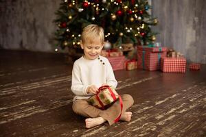 Cute little boy sitting on the floor in front of the Christmas tree with gifts photo