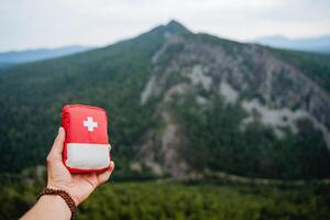 demonstration of a first aid kit on a hike, a hand holding a first aid kit, a red bag with medicines against the background of mountains, equipment on a hike. photo