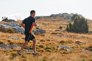 Determined Athlete Running Through Rugged Mountain Terrain at Sunrise. photo