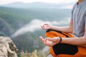 A yogi sits in the lotus position on top of a mountain. A fragment of a part of the human body in a posture of relaxation and immersion in meditation in nature, Zen in the mountains. photo