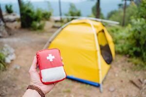 First aid kit in the mountains, extreme set of medicines, red first aid kit on the background of the tent, equipment on a hike, hand holding a minibag with medicines photo