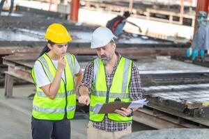 Engineer and female foreman team checking project at precast concrete factory site, Caucasian engineer and worker in hardhats discussing on construction site photo