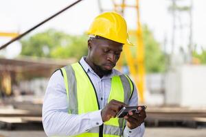 ingeniero hombre en sombreros duros utilizando móvil teléfono inteligente en construcción sitio, capataz trabajador a prefabricado fábrica sitio foto