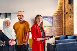 A group of young business colleagues, including a woman in a hijab, stands united in the modern corridor of a spacious startup coworking center, representing diversity and collaborative spirit. photo