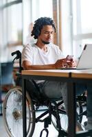 An African American businessman in a wheelchair takes a work break, using his smartphone while seated in a modern business startup coworking center, reflecting both inclusion and technology photo
