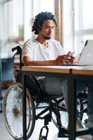 An African American businessman in a wheelchair takes a work break, using his smartphone while seated in a modern business startup coworking center, reflecting both inclusion and technology photo