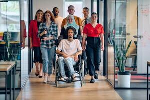 A diverse group of young business people congregates within a modern startup's glass-enclosed office, featuring inclusivity with a person in a wheelchair, an African American young man, and a hijab photo