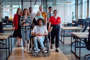 A diverse group of young business people congregates within a modern startup's glass-enclosed office, featuring inclusivity with a person in a wheelchair, an African American young man, and a hijab photo