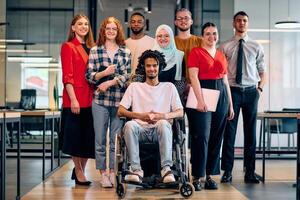 A diverse group of young business people walking a corridor in the glass-enclosed office of a modern startup, including a person in a wheelchair and a woman wearing a hijab photo