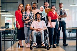 A diverse group of young business people walking a corridor in the glass-enclosed office of a modern startup, including a person in a wheelchair and a woman wearing a hijab photo