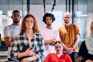 A diverse group of young business people walking a corridor in the glass-enclosed office of a modern startup, including a person in a wheelchair and a woman wearing a hijab photo