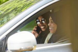 Two Muslim women wearing hijab converse on a smartphone while traveling together in a car through the photo