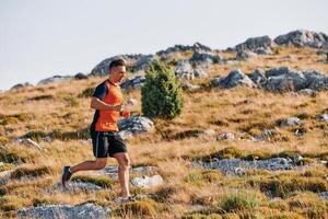 Determined Athlete Running Through Rugged Mountain Terrain at Sunrise. photo