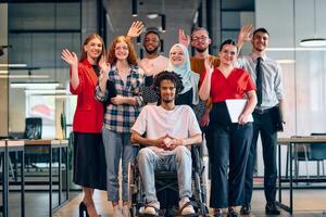 A diverse group of young business people walking a corridor in the glass-enclosed office of a modern startup, including a person in a wheelchair and a woman wearing a hijab photo