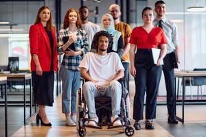 A diverse group of young business people walking a corridor in the glass-enclosed office of a modern startup, including a person in a wheelchair and a woman wearing a hijab photo