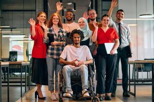 A diverse group of young business people walking a corridor in the glass-enclosed office of a modern startup, including a person in a wheelchair and a woman wearing a hijab photo