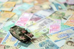 Small green tank on many banknotes of different currency. Background of war funding photo