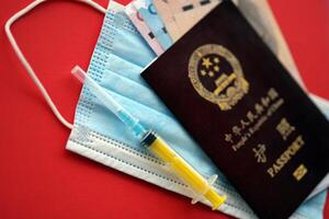 Red passport of People Republic of China and chinese yuan money bills with syringe and mask photo