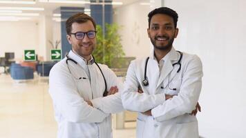 Portrait of two multiracial doctors smiling and looking at camera. Indian and caucasian smiling doctors in white coat working in an office and looking at camera video