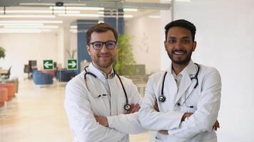 Portrait of two multiracial doctors smiling and looking at camera. Indian and caucasian smiling doctors in white coat working in an office and looking at camera video