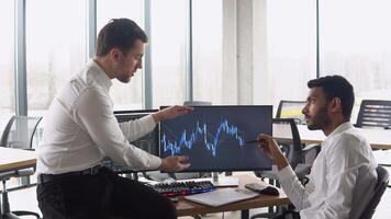 Two multiracial investors brokers analysing indexes online cryptocurrency stock. Diverse managers traders analysts discussing financial growth market at desk with pc graphs on screen video