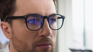Crypto trader wearing eyeglasses working looking at computer screen reflecting in glasses analyzing online trading stock exchange market financial data charts. Close up eye in spectacles reflection video