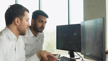 Two multiracial investors brokers analysing indexes online cryptocurrency stock. Diverse managers traders analysts discussing financial growth market at desk with pc graphs on screen video