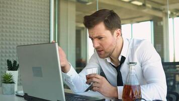 Very drunk businessman with a glass of whiskey in his hands yelling into a laptop at a business partner video